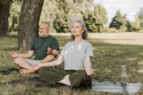 Healthy and mature couple reducing stress by meditating in nature